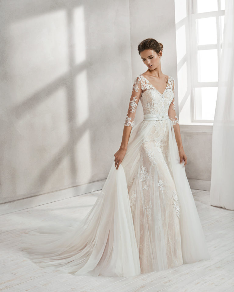 Mermaid-style beaded lace wedding dress with three-quarter sleeves, V-neckline, low back and tulle overskirt, in nude and natural.