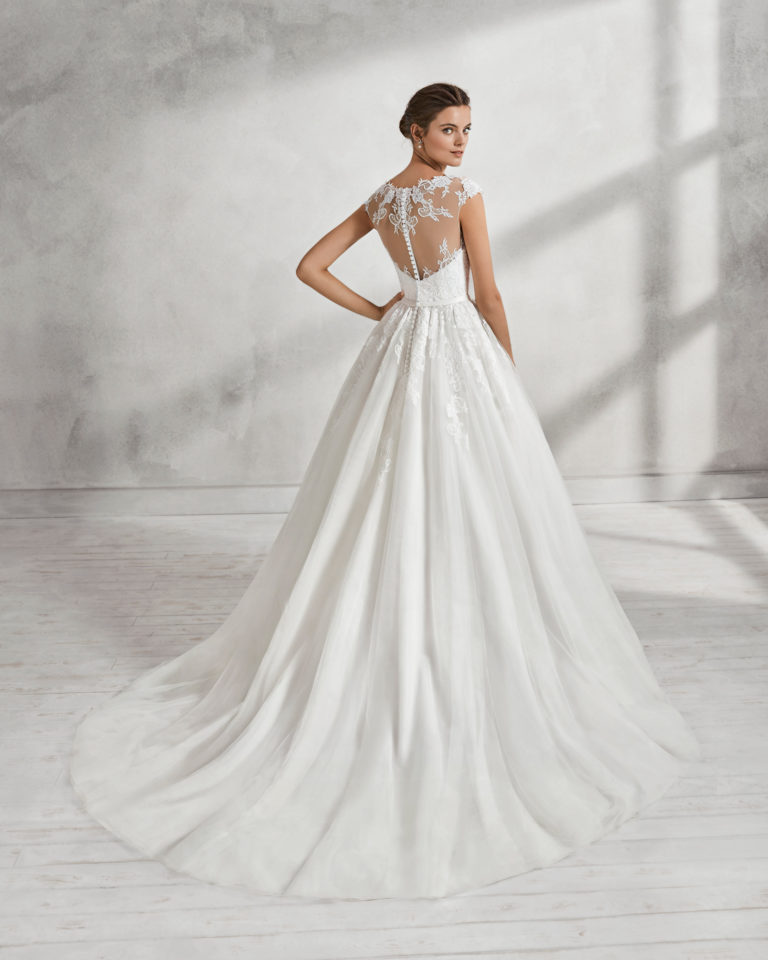 Vestido de novia estilo romántico en tul y encaje con escote ilusión con espalda escotada en color natural y blanco con aplicaciones de pedrería.