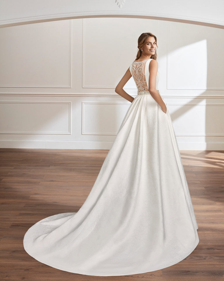 Vestido de novia estilo clásico en brocado y pedreria. Escote barco con espalda y apliques de pedreria con bolsillos.