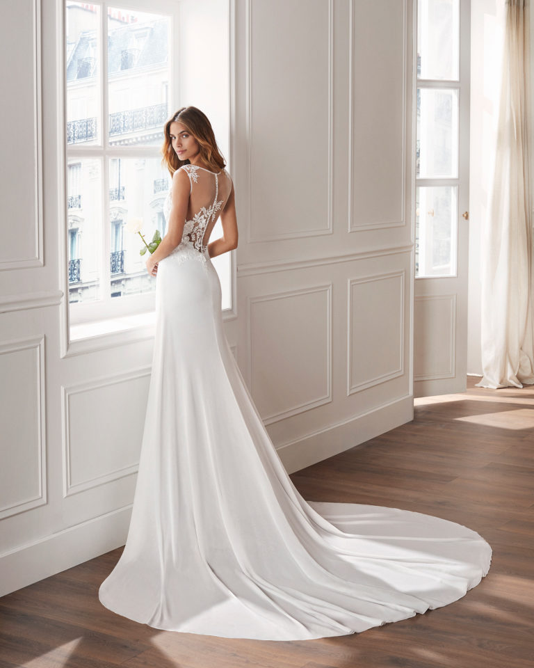 Sheath-style wedding dress in crepe Georgette. Sleeveless lace bodice with illusion neckline and train. Available in natural. 2019  Collection.
