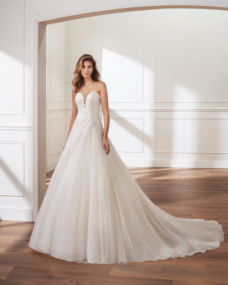 Vestido de novia corte linea A en garza. Escote en V profundo, cuerpo de encaje y falda de pliegues. Disponible en color natural. Colección  2019.