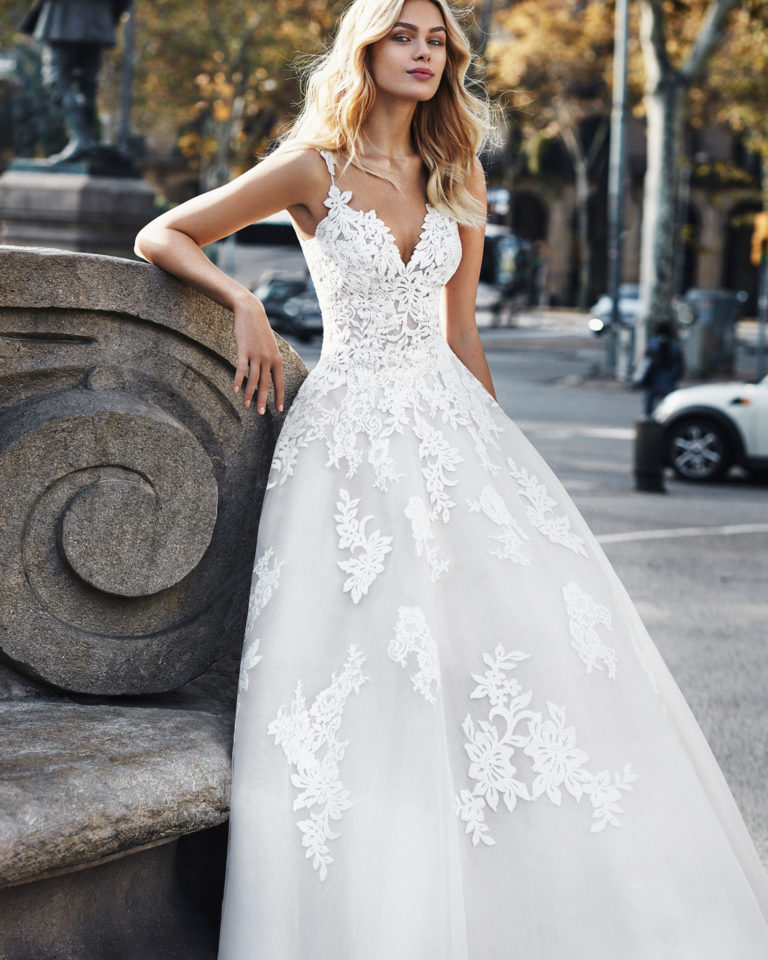 Lace princess-style wedding dress. Deep-plunge sweetheart neckline, straps, and skirt with beaded lace appliqués. Available in natural/nude and natural. 2019 Collection.