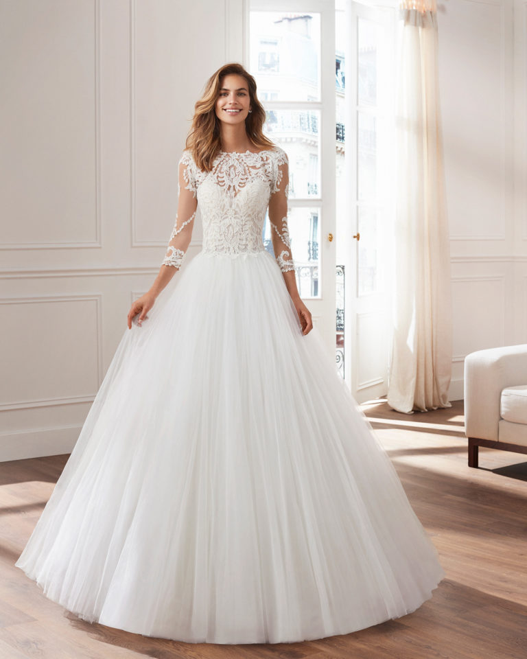 Vestido de novia estilo princesa en tul y encaje. Escote ilusión, cuerpo bordado de encaje pedrería y manga larga. Disponible en color natural. Colección  2019.