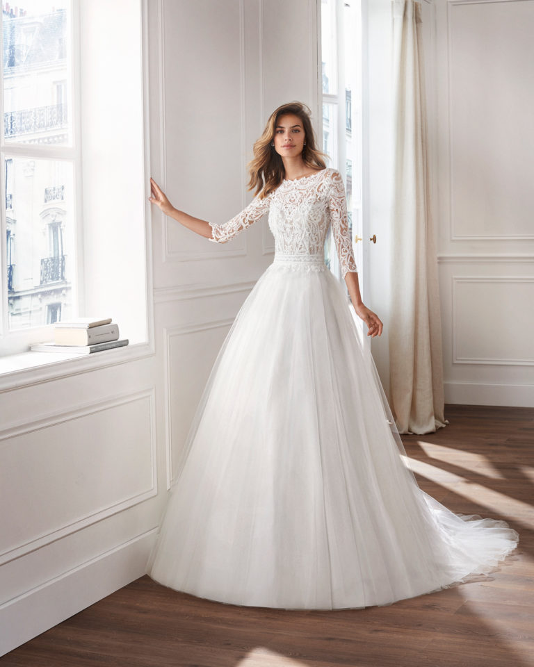 Vestido de novia estilo princesa en tul. Escote ilusión, cuerpo de encaje pedrería y manga larga. Disponible en color natural. Colección  2019.
