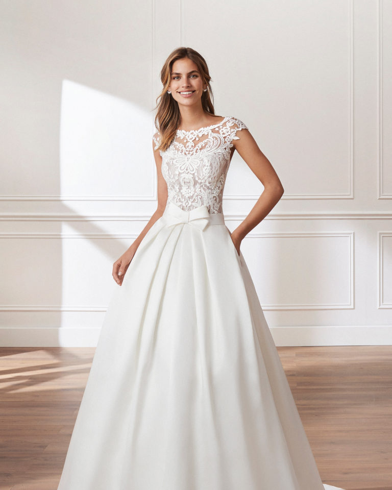 Classic A-line mikado wedding dress. Beaded lace bodice with bateau neckline, short sleeves and pleats at the waist. Available in natural. 2019  Collection.