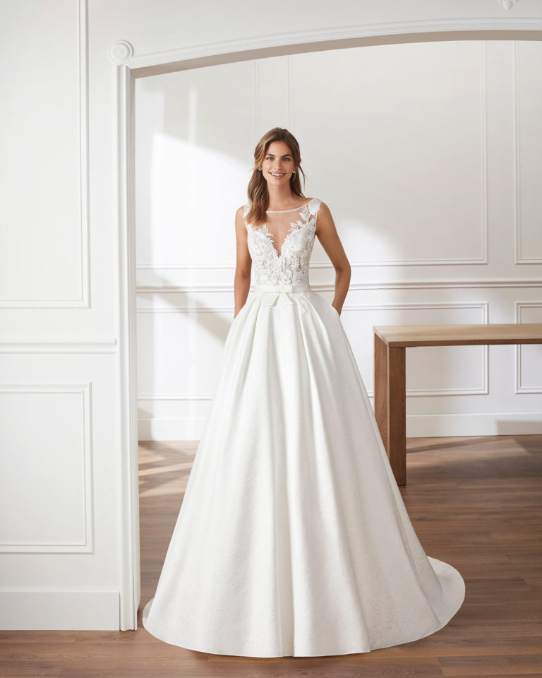 Classic A-line brocade wedding dress. Deep-plunge V-neckline with illusion overlay and beaded lace bodice. Available in natural. 2019  Collection.