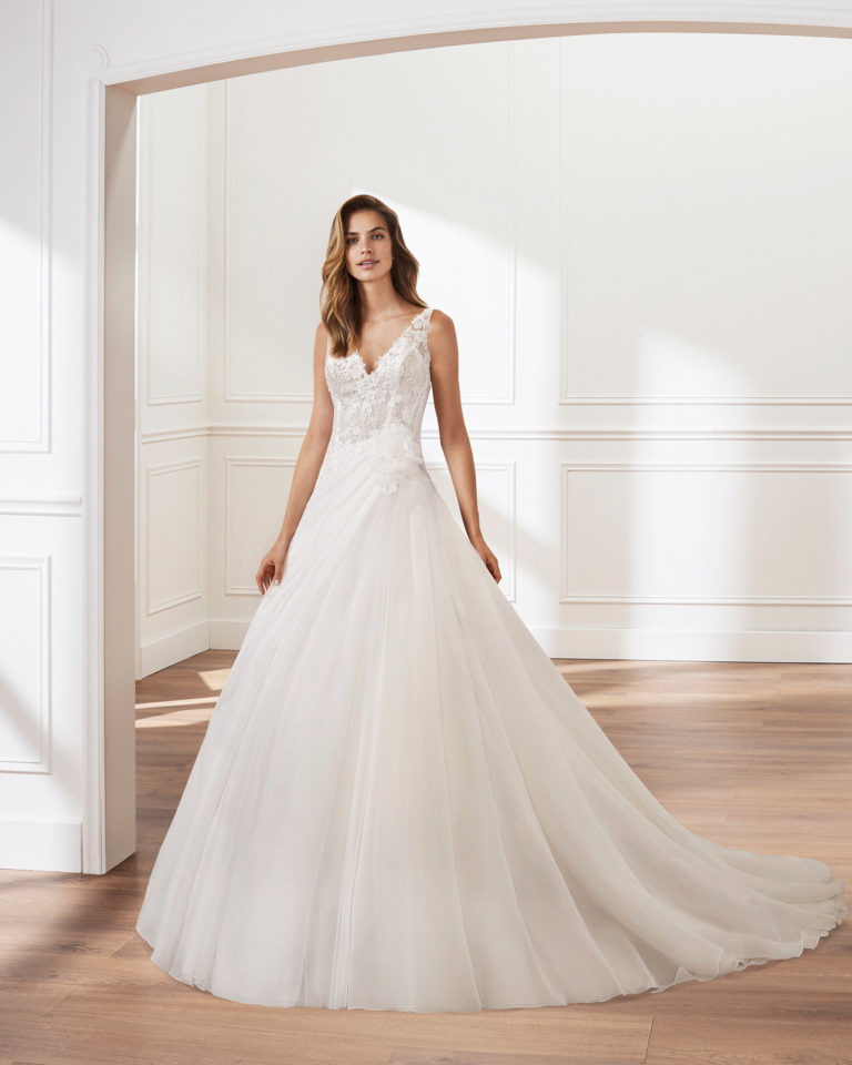 Vestido de novia corte linea A en garza. Escote en V, cuerpo de encaje y falda de pliegues. Disponible en color natural. Colección  2019.
