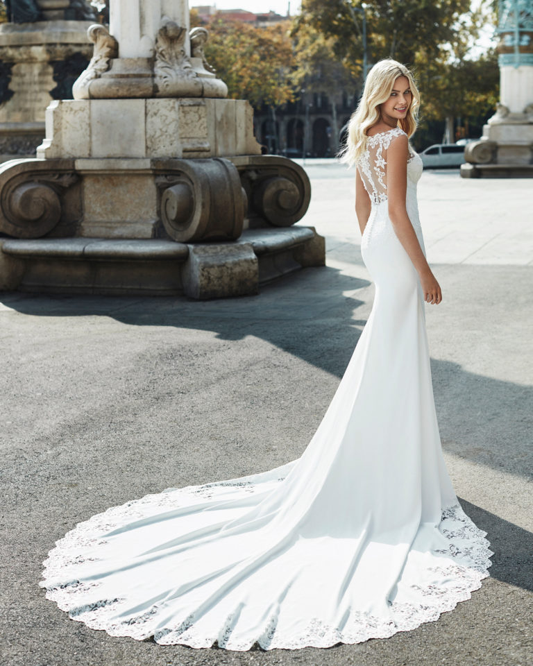 Sheath-style wedding dress in crepe. Sleeveless beaded lace bodice with illusion neckline and train edged with lace. Available in natural. 2019  Collection.