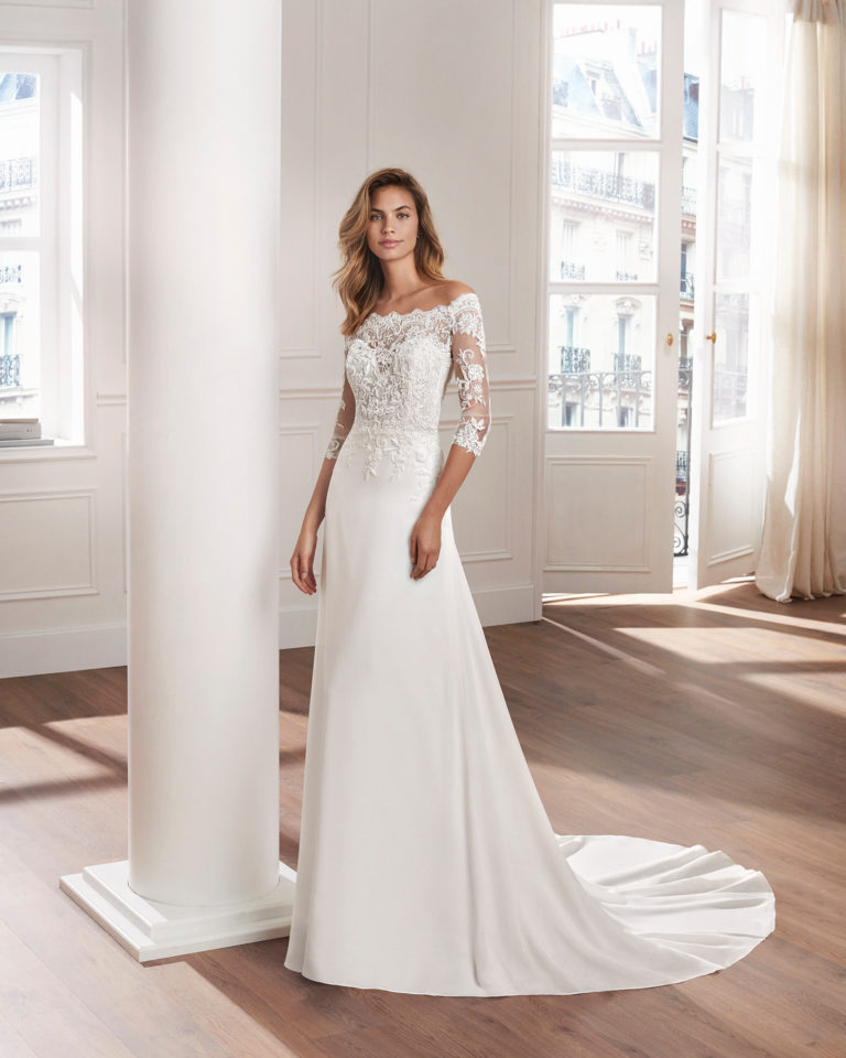 Sheath-style wedding dress in crepe Georgette. V-neck beaded lace bodice with long sleeves and train. Available in natural. 2019  Collection.