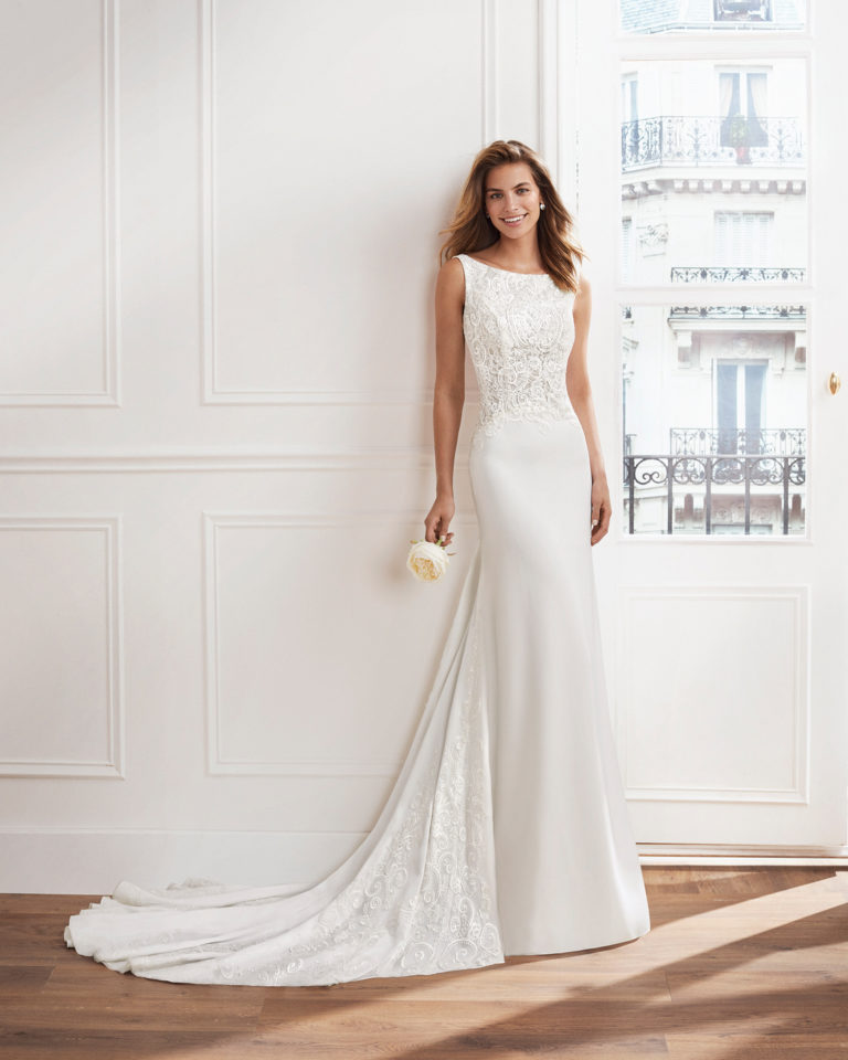 Vestido de novia corte recto en georgette. Cuerpo de encaje con pedrería, escote barco y arrastre con encaje pedrería incrustado. Disponible en color natural. Colección  2019.