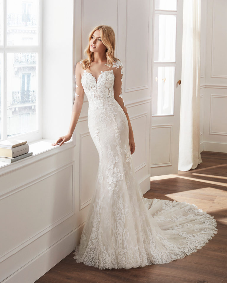 Mermaid-style wedding dress in beaded lace. Illusion neckline, long sleeves and appliquéd skirt. Available in natural and natural/nude. 2019  Collection.