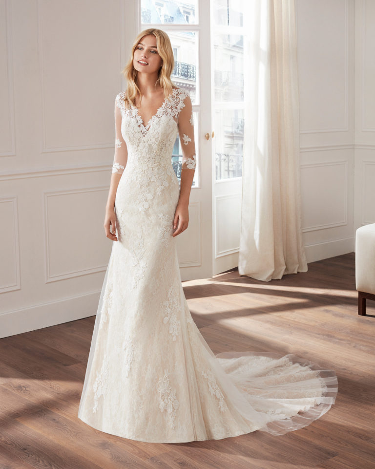 Vestido de novia corte sirena de encaje. Escote en V, manga larga de tul y falda de aplicaciones. Disponible en color natural y natural/champagne. Colección  2019.