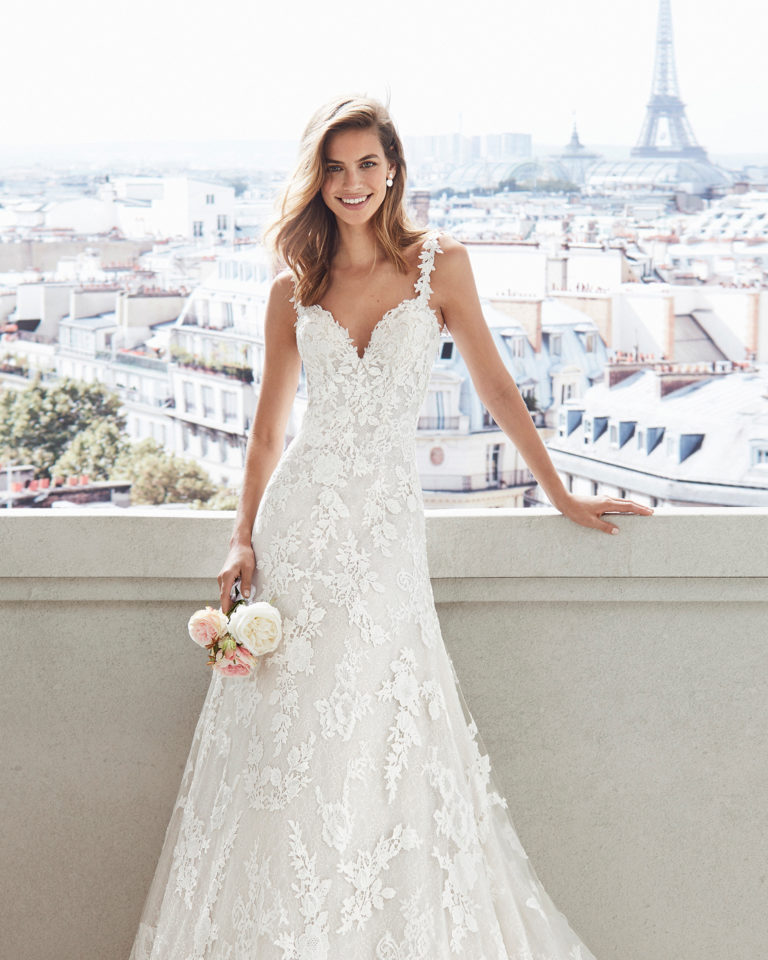 Sheath-style wedding dress in lace. V-neckline and appliquéd skirt. Available in natural/nude and natural. 2019 Collection.