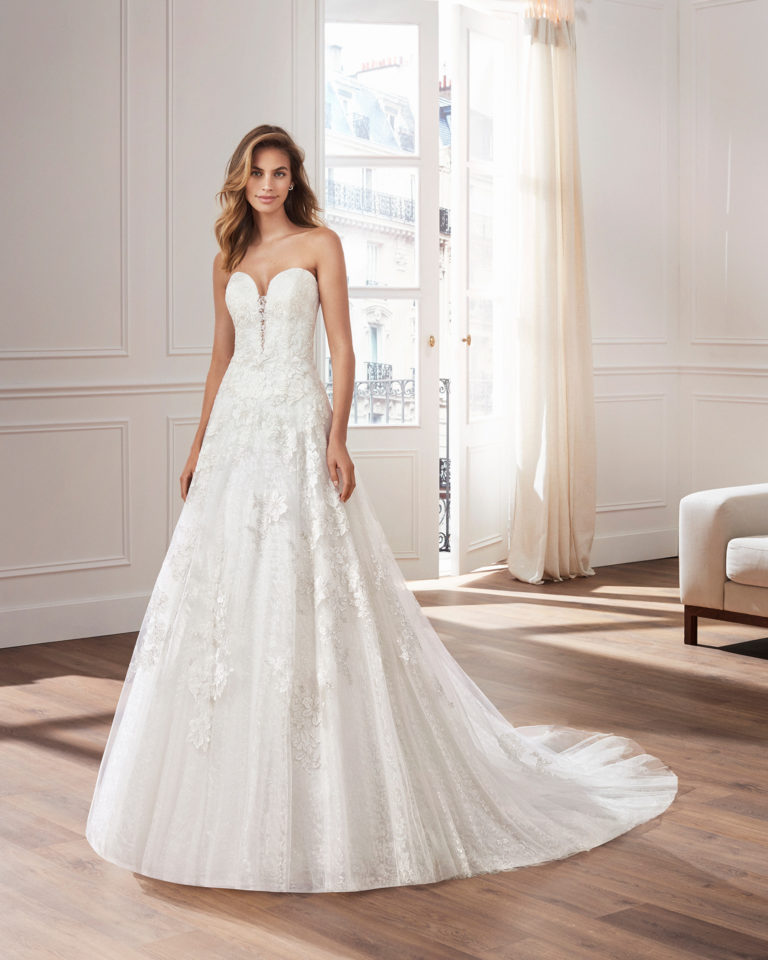 Vestido de novia corte evasé de encaje. Escote corazón, tirantes y aplicaciones en falda. Disponible en color natural. Colección  2019.