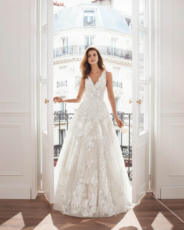 Vestido de novia corte evasé de encaje. Escote en V, tirantes y aplicaciones de encaje con pedrería en falda. Disponible en color natural. Colección  2019.