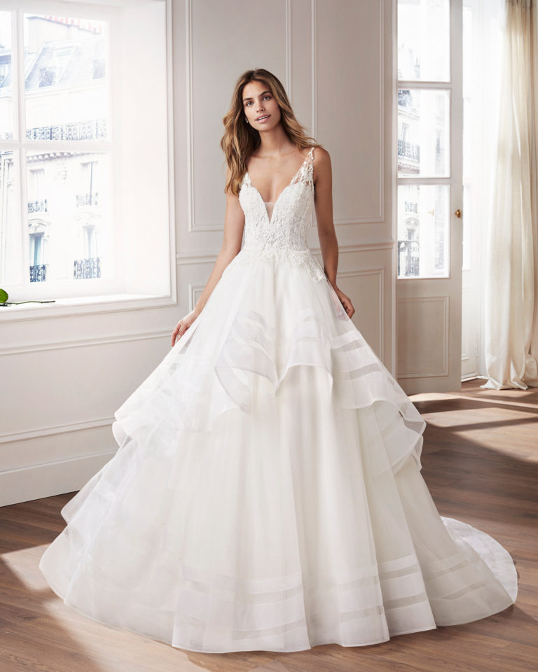 Vestido de novia estilo princesa en tul y encaje. Escote en V, cuerpo bordado de encaje pedrería y falda de volantes de tul. Disponible en color natural. Colección  2019.