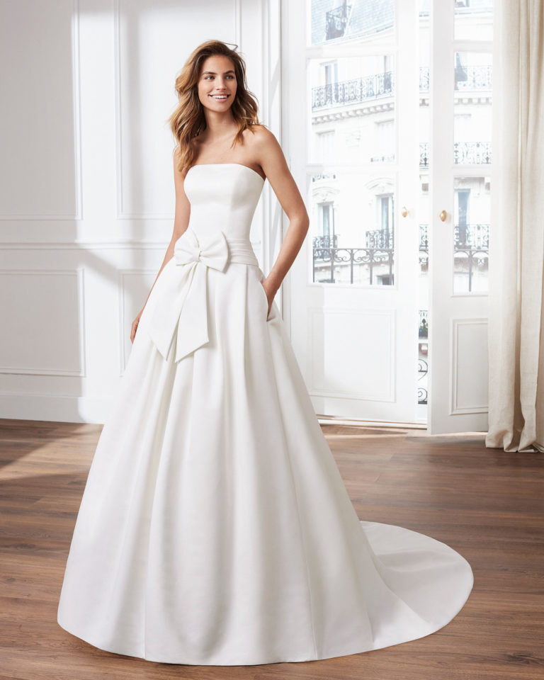Vestido de novia estilo clásico línea A en otomán. Escote palabra de honor y lazo en cintura. Disponible en color natural. Colección  2019.