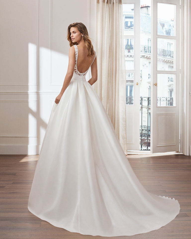 Vestido de novia estilo clásico línea A en mikado. Escote barco con pedrería en hombros y espalda joya. Disponible en color natural. Colección  2019.