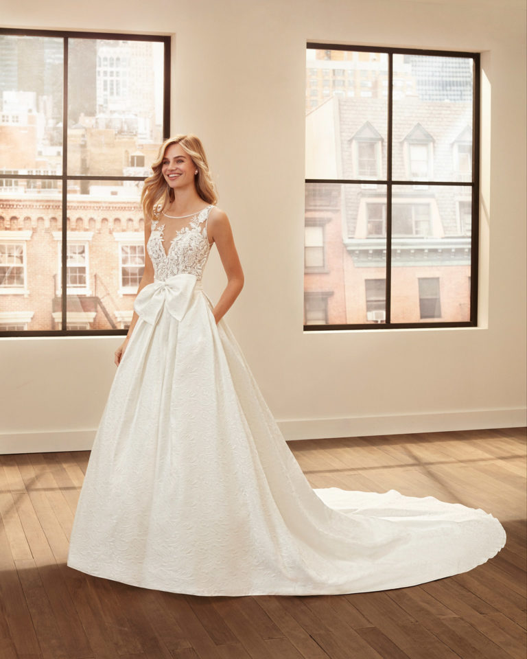 Vestido y sobrefalda de novia estilo clásico de brocado, crep, encaje y pedrería con escote y espalda con transparencias. Colección 2020.