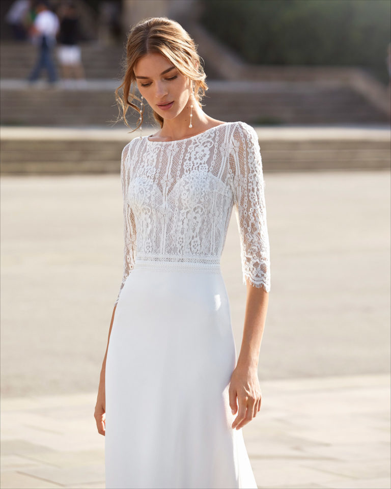 Sheath-style wedding dress in stretch crepe and lace with beading on waist. Bateau neckline with sweetheart underlay, V-back and three-quarter sleeves. 2021  Collection.