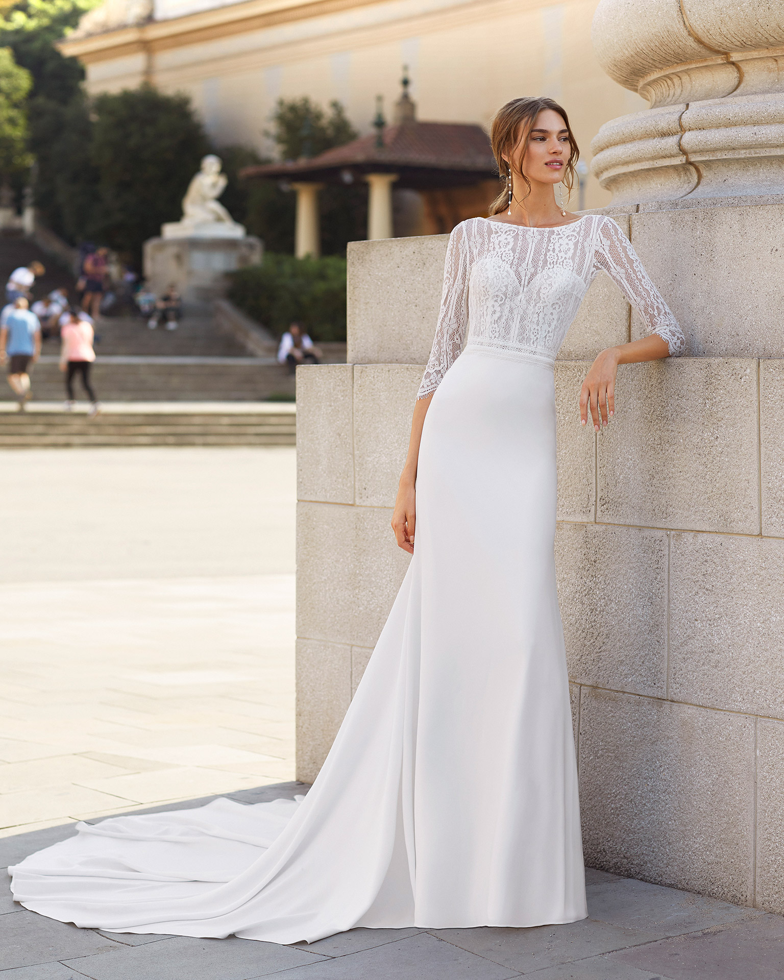 Sheath-style wedding dress in stretch crepe and lace with beading on waist. Bateau neckline with sweetheart underlay, V-back and three-quarter sleeves. 2021  Collection.