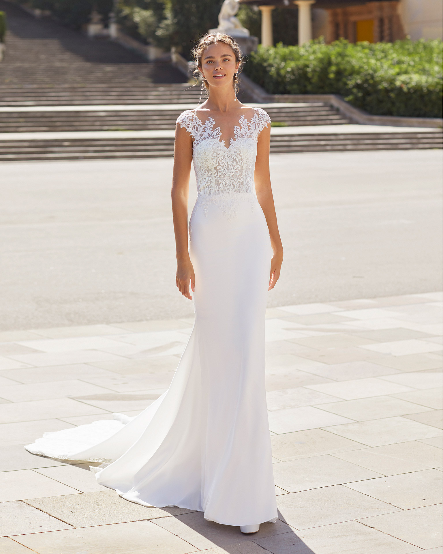 Sheath-style wedding dress in stretch crepe and lace. Bateau neckline with sweetheart underlay, low back, short sleeves with appliqués and trefoil train. 2021  Collection.