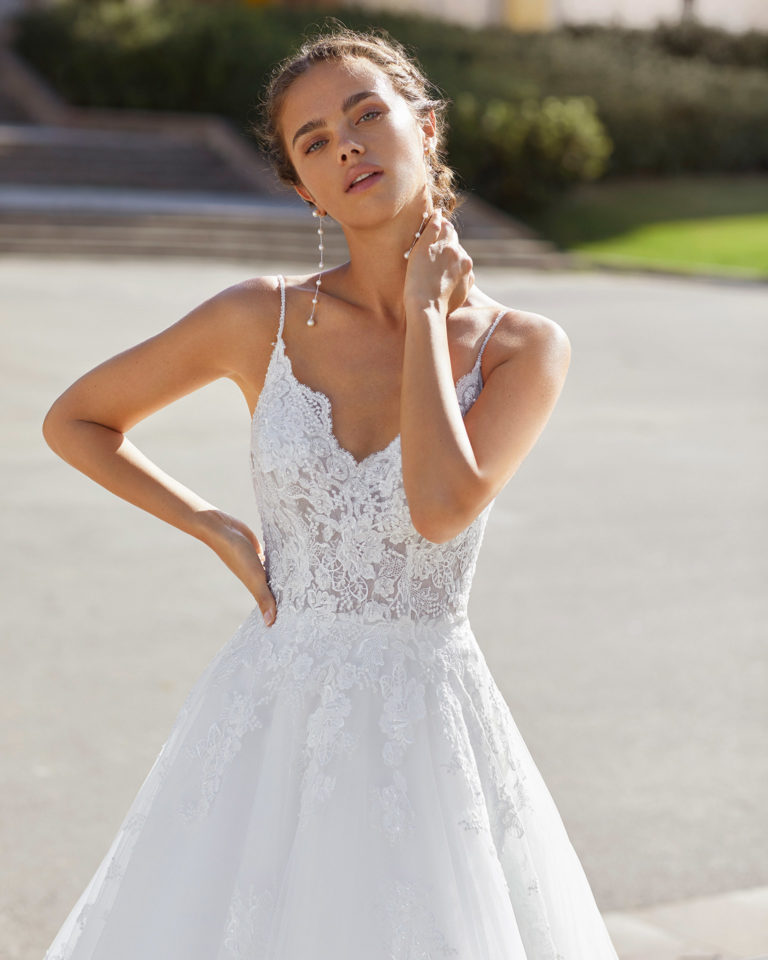 Romantic-style wedding dress in tulle and beaded lace. V-neckline and low back with spaghetti shoulder straps. 2021 Collection.