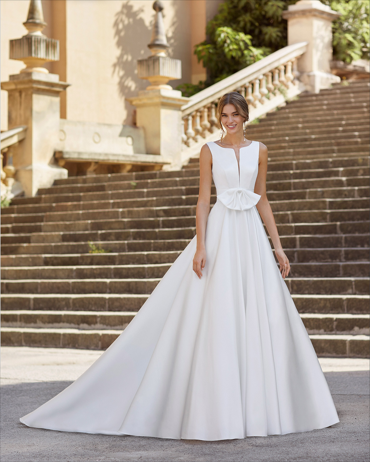 Classic-style wedding dress in satin. Deep-plunge neckline and U-back, with front bow at waist and pockets. 2021  Collection.