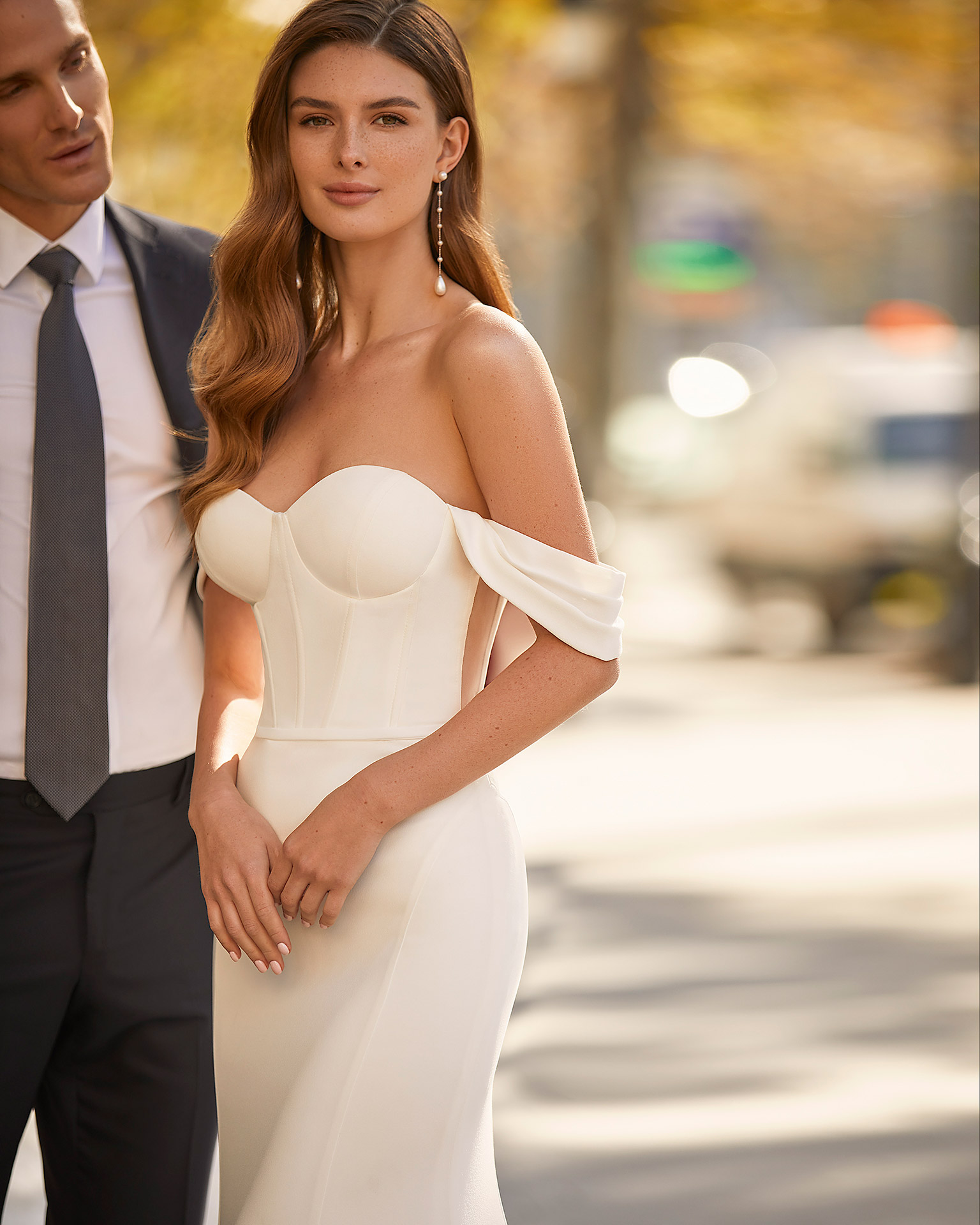 Modern sheath-style wedding dress, made of stretch crepe, with detachable sleeves; with a push-up corset structure, a button-up sheer back, and dropped pleated sleeves. Trendy Luna Novias outfit made of stretch crepe. LUNA_NOVIAS.