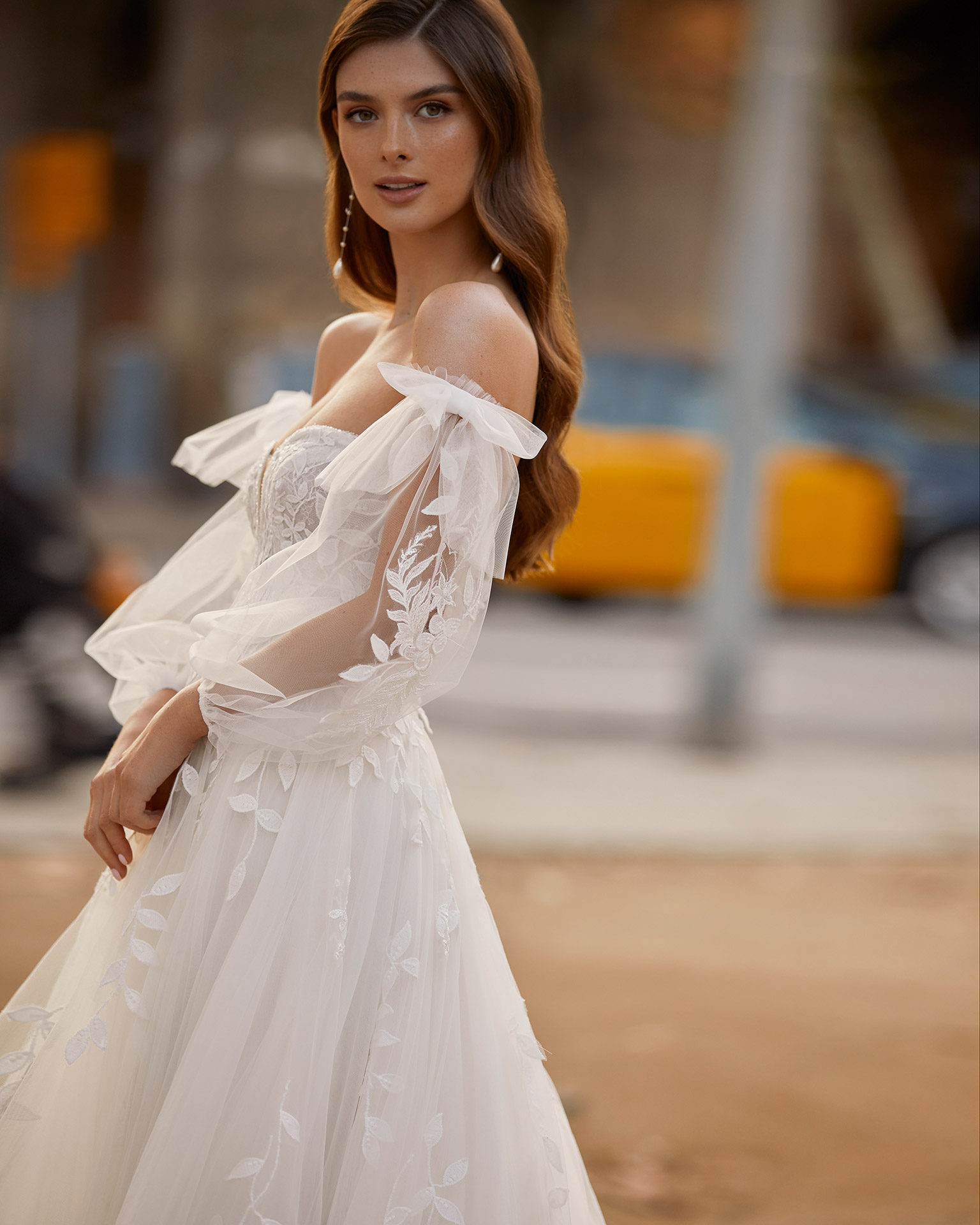 Romantic princess-style wedding dress, made of tulle and lace appliqués, with a sheath-style skirt with flounces; with a deep-plunge neckline with delicate beadwork detail, an open back, and voluminous tulle sleeves. Unique Luna Novias outfit made of tulle with lace appliqués. LUNA_NOVIAS.