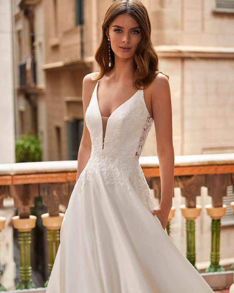 Classic-style wedding dress, made of satin, with lace appliqués on the bodice; with a deep-plunge neckline, a plunging lace back, and straps. Unique Luna Novias look made of satin combined with lace. LUNA_NOVIAS.