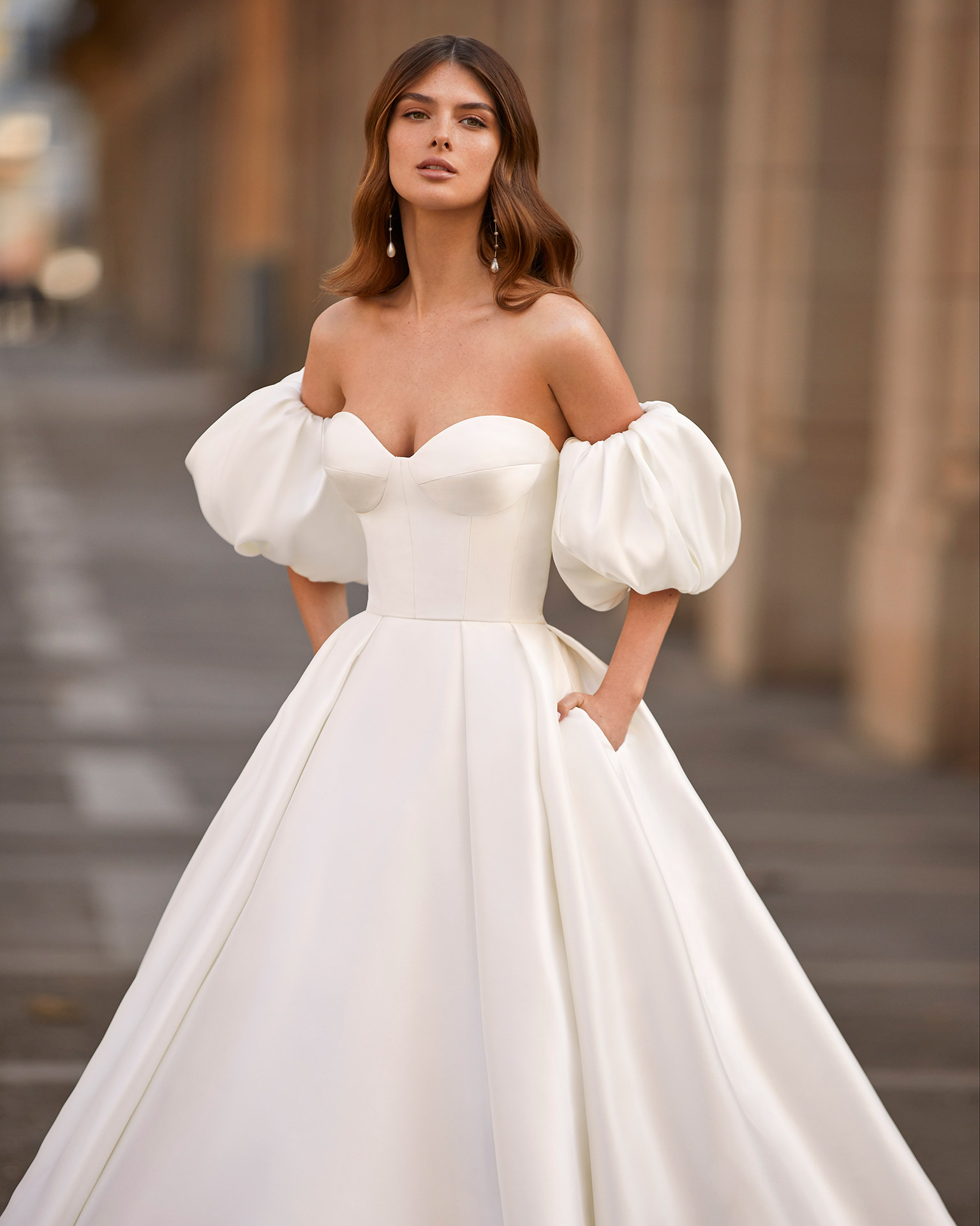 Classic princess-style wedding dress, made of matt Mikado, with a voluminous sheath-style skirt; with a strapless neckline, a buttoned back down to the end of the train, and puffed sleeves. Dreamy Luna Novias dress made entirely of Mikado. LUNA_NOVIAS.