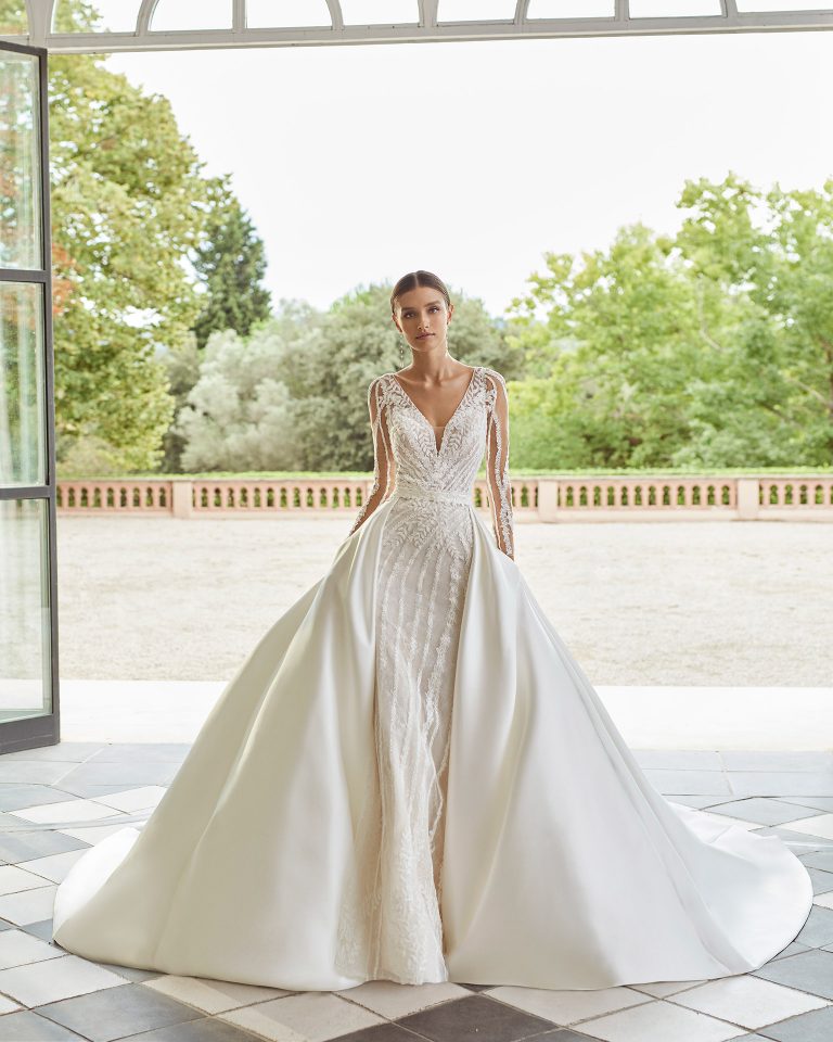 Vestido de novia dos piezas de corte evasé, con sobrefalda con botones hasta el largo de la falda; de escote deep-plunge con detalle de canutillos bordados, espalda con transparencias abotonada y con manga larga. Conjunto Luna Studio delicado de confección en tul y encaje enriquecido con pedrería y mikado. LUNA_NOVIAS.