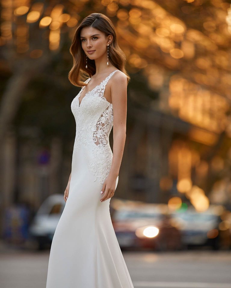 Sexy sheath-style wedding dress, made of stretch crepe, with a buttoned skirt throughout the train; with a V-neckline and tattoo-effect open back. Dreamy Luna Novias design made of stretch crepe combined with beadwork lace. LUNA_NOVIAS.