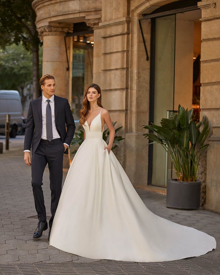 Classic-style wedding dress, made of satin, featuring a full buttoned skirt; with a deep-plunge neckline, a V-back, and straps. Dreamy Luna Novias look made entirely of satin. LUNA_NOVIAS.
