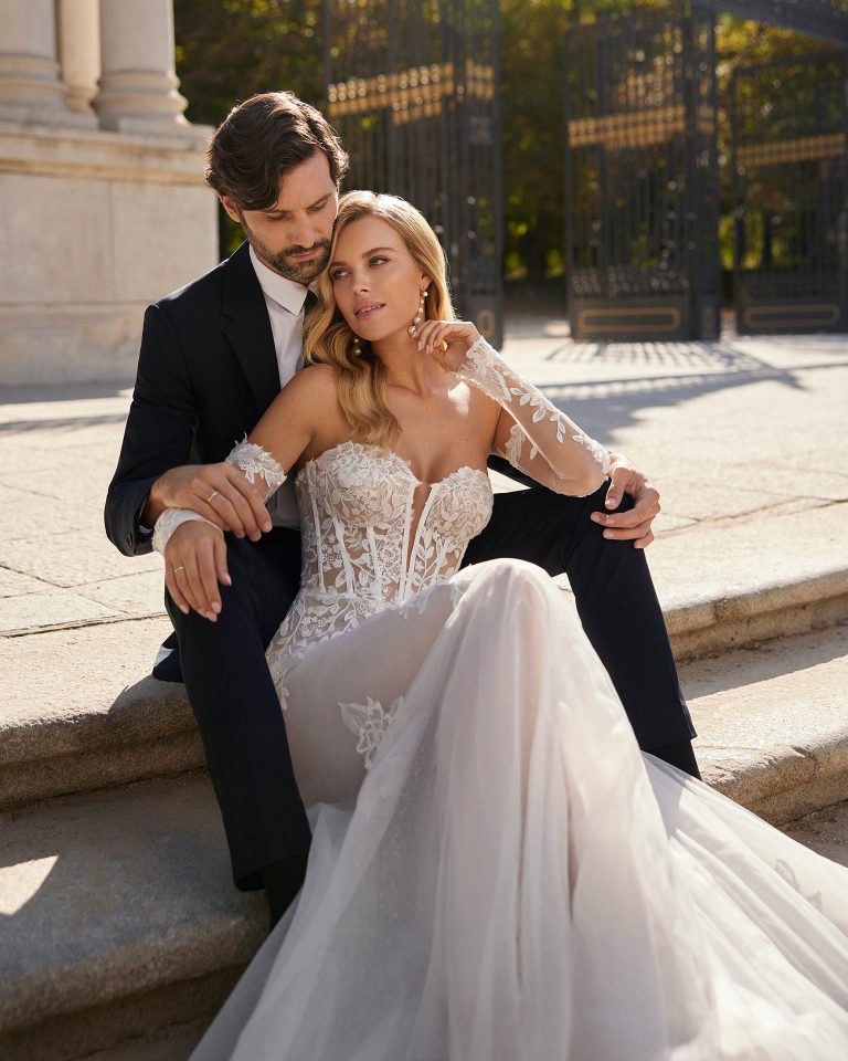Vestido de novia largo de estilo elegante, elaborado con tul combinado con encaje y pedrería. Presenta un escote corazón, una espalda cerrada y manga larga extraíble. Un look de tendencia Luna Novias. LUNA_NOVIAS.