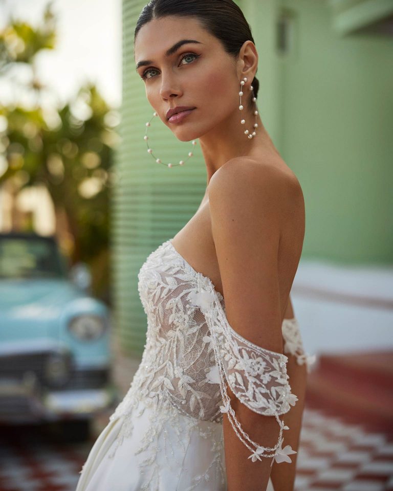 Vestido de novia largo de corte volumen. Raso, escote palabra de honor, tirantes caídos, espalda escotada y falda con abertura lateral. LUNA_NOVIAS.