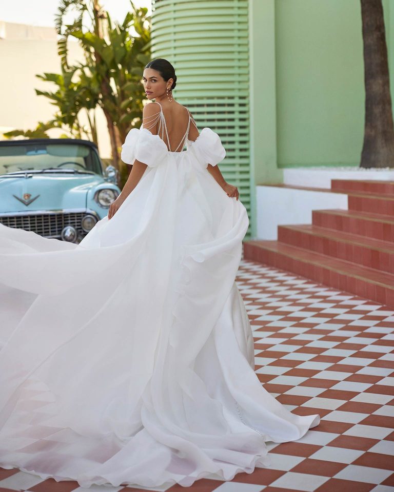 Vestido de novia largo de dos piezas con corte volumen. Mikado, escote pico, tirantes de pedrería, espalda escotada y capa. LUNA_NOVIAS.
