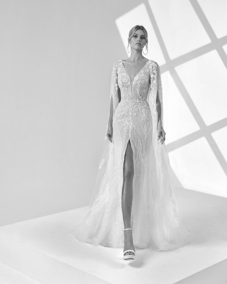 Vestido de novia largo de dos piezas con corte sirena. Encaje y pedrería, escote pico, espalda en V y falda con abertura central y capa. LUNA_NOVIAS.