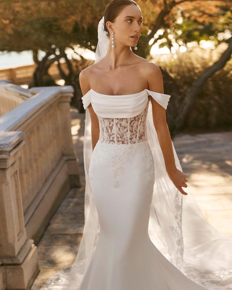 Mermaid silhouette wedding dress with sweetheart neckline and short off-shoulder sleeves. Lace bodice with beadwork and stretch mikado skirt with appliqués. LUNA_NOVIAS.