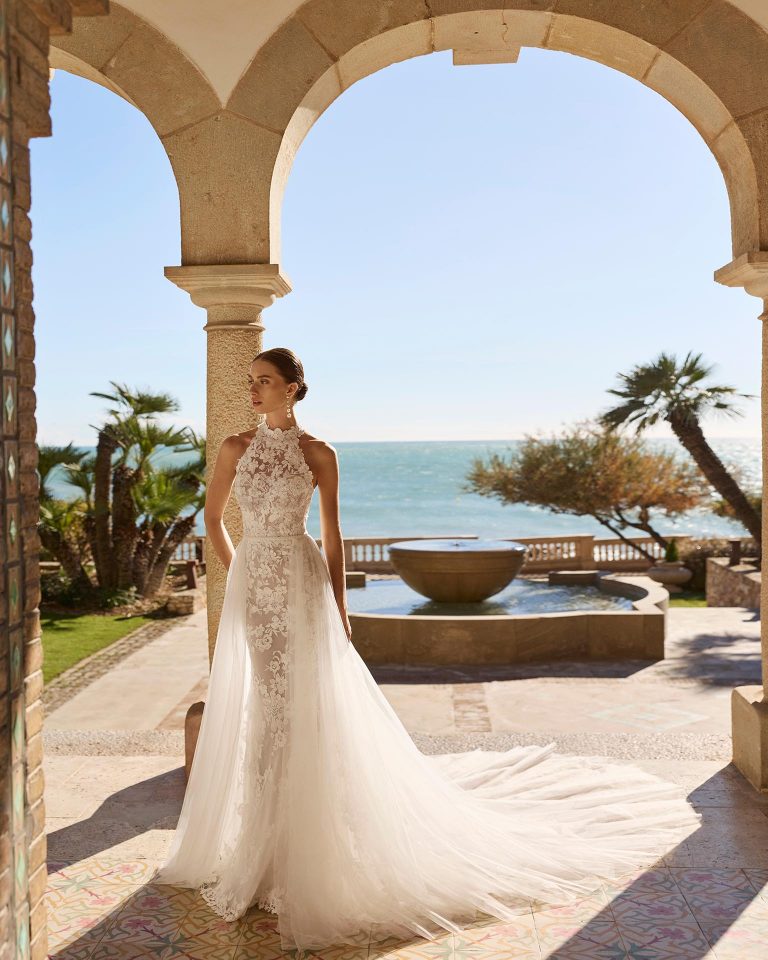 Two-piece lace wedding dress with mermaid silhouette. Halter neckline and open back. Bodice with beadwork, skirt with appliqués and beadwork. Includes tulle overskirt. LUNA_NOVIAS.