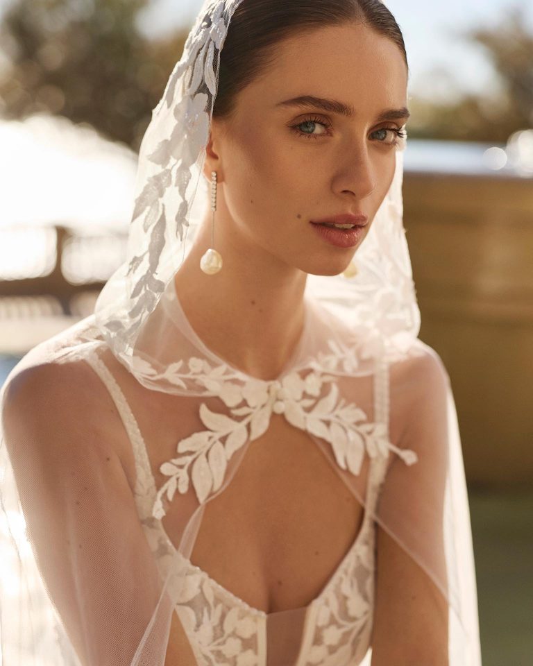 Two-piece mermaid silhouette wedding dress with lace. Deep neckline, straps, V-back. Appliqués on bodice and skirt and beadwork on bodice. Tulle and lace layer with hood. LUNA_NOVIAS.