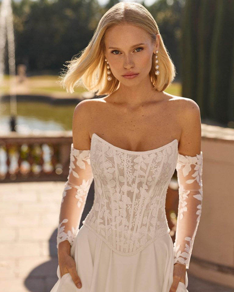 Two-piece wedding dress with sweetheart neckline. Lace bodice with beading and corset. Off-shoulder long sleeves with appliqués. Plain crepe satin skirt. LUNA_NOVIAS.