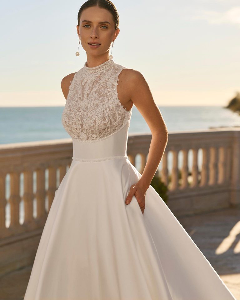 Wedding dress with halter neckline, beaded lace bodice, open back and A-line silhouette with mikado skirt. LUNA_NOVIAS.
