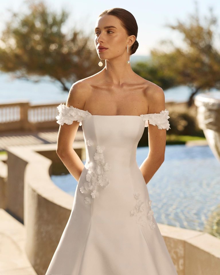 Two-piece bridal gown in A-line silhouette made of elastic mikado. Off-the-shoulder neckline with off-shoulder straps. Floral embellishments and beadwork. Removable Verona mikado collar. LUNA_NOVIAS.