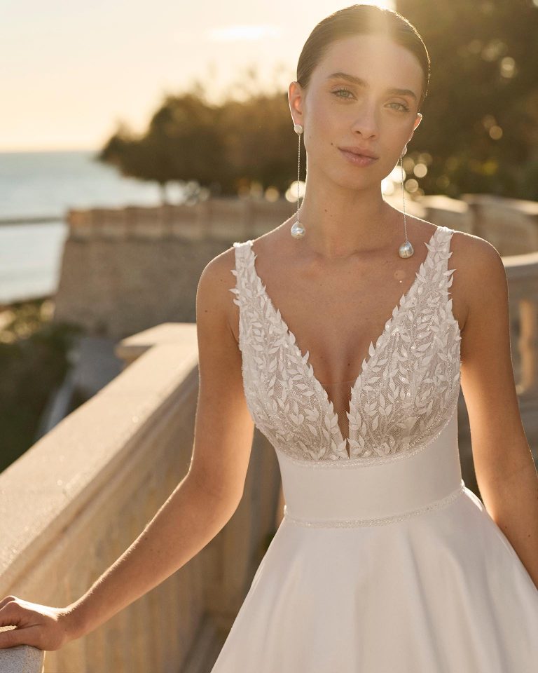 Wedding dress with V-neckline and straps. Lace bodice with beading and V-back. A-line skirt in mikado with bow. LUNA_NOVIAS.