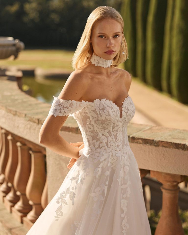 A-line wedding dress with sweetheart neckline and off-shoulder straps. Beaded lace bodice, glitter tulle skirt with lace appliqués. Includes choker. LUNA_NOVIAS.