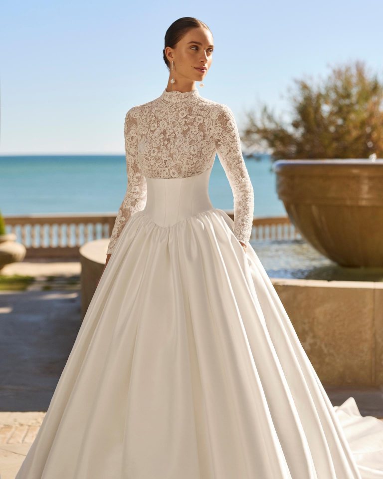 Princess silhouette wedding dress with swan neckline and long lace sleeves. Lace bodice with beading, mikado skirt and back opening. LUNA_NOVIAS.