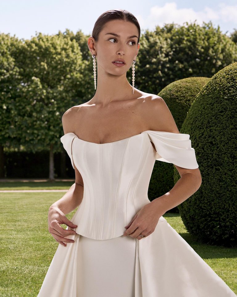 Three-piece wedding dress in mikado with mermaid silhouette, sweetheart neckline, detachable off-shoulder sleeves, corset closure and mikado overskirt. LUNA_NOVIAS.