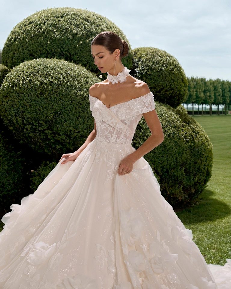Princess silhouette wedding dress with off-the-shoulder neckline and sleeves. Beaded lace bodice and glitter tulle skirt. Includes lace choker. LUNA_NOVIAS.